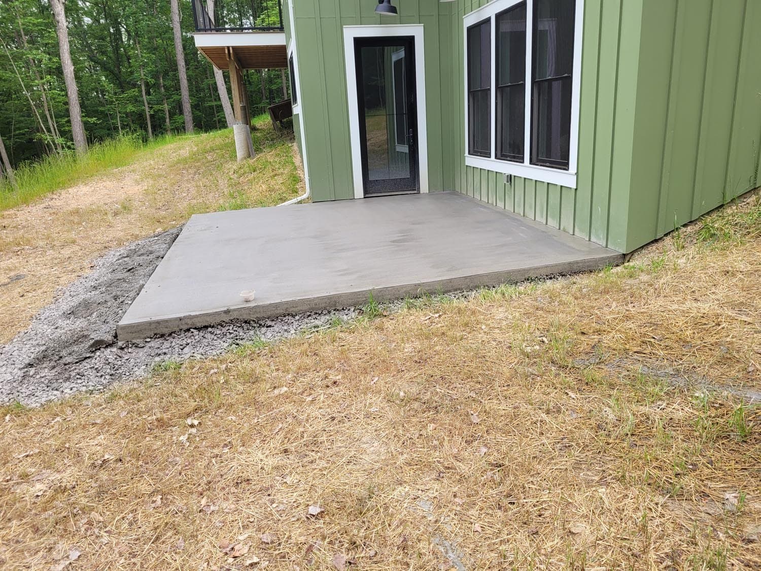 Newly poured concrete patio slab at green sided house entrance surrounded by gravel