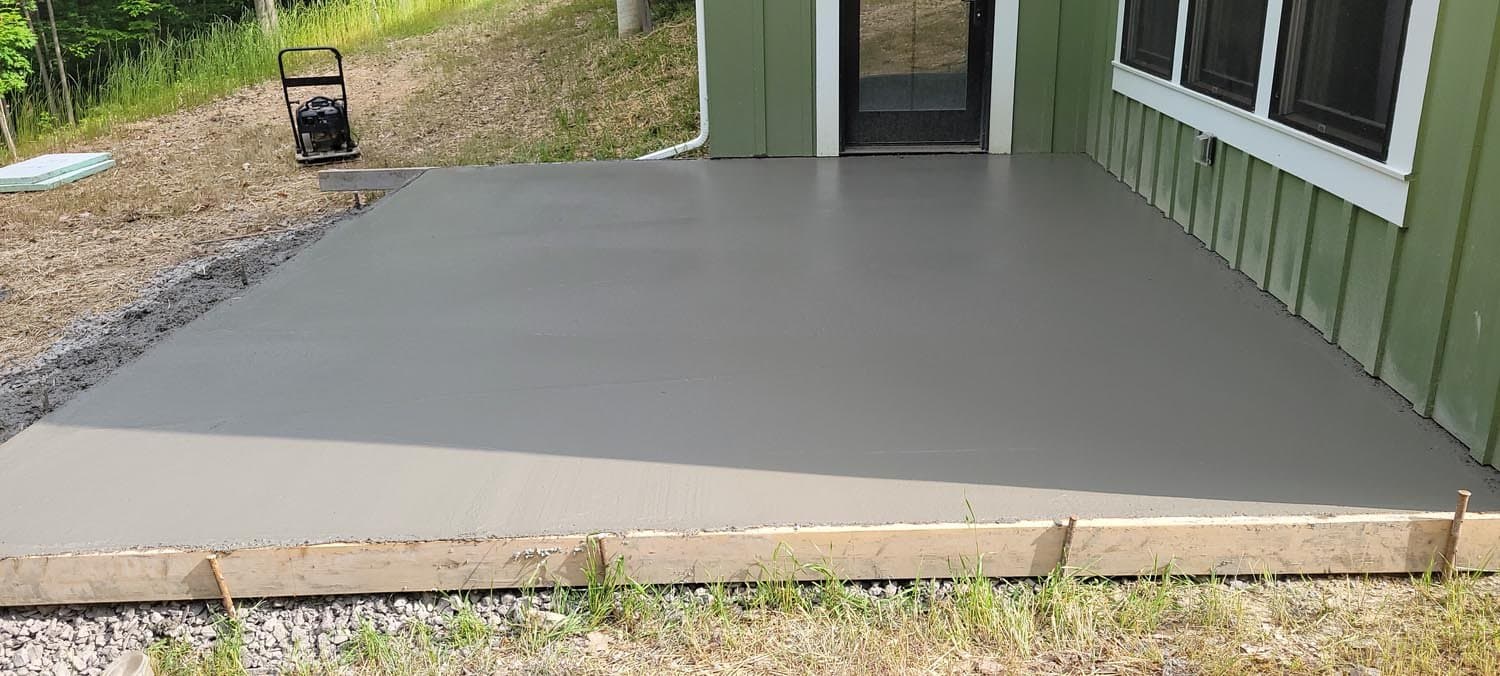Smooth gray concrete patio with wooden forms outside green building entrance