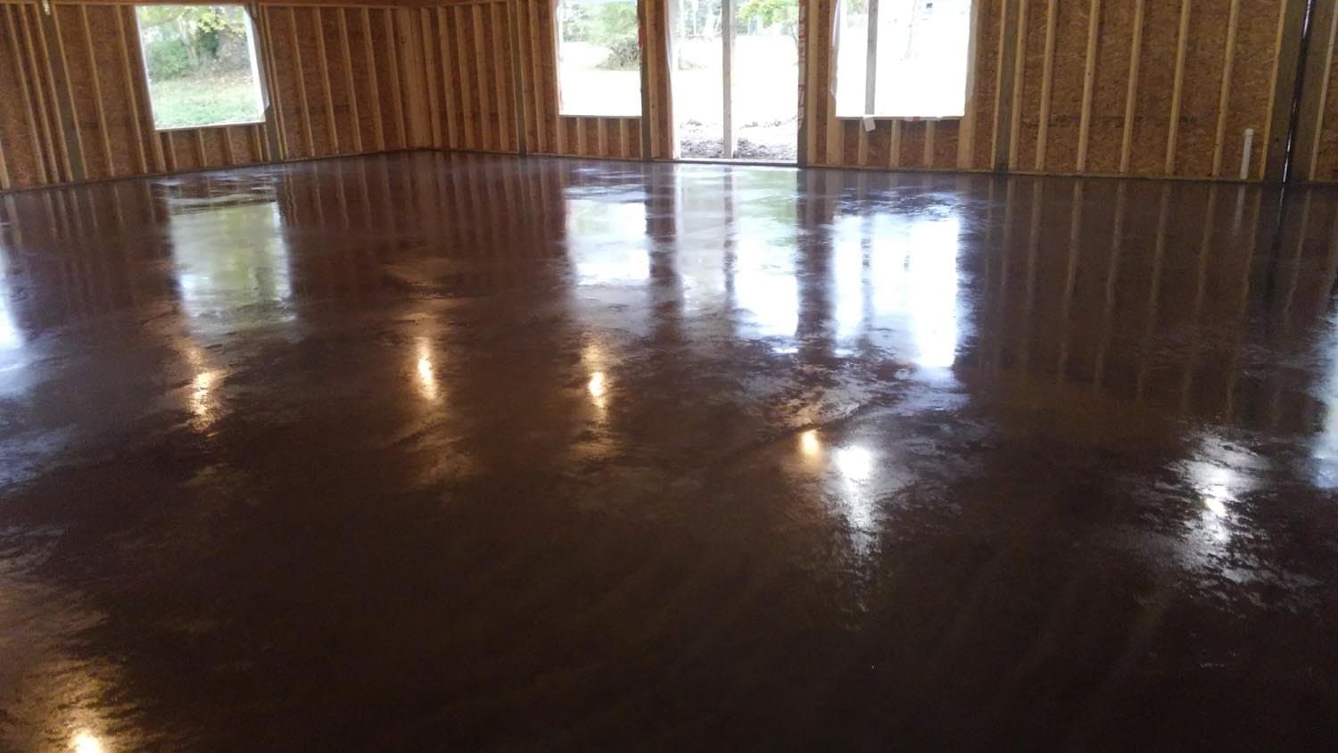 Polished concrete floor in open room with exposed wood framing and windows