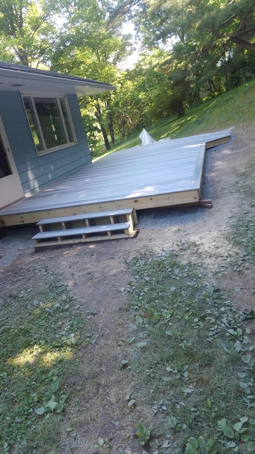 Wooden deck under construction attached to blue house with steps and gravel base