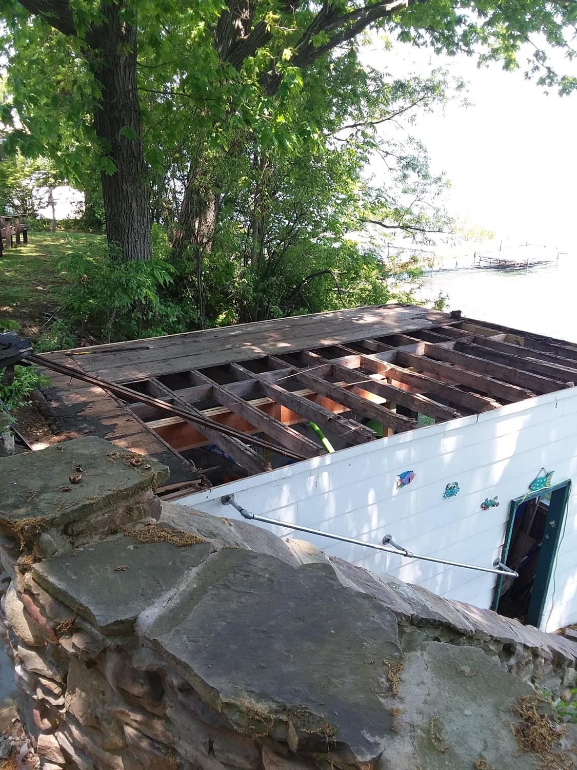 Demolished deck structure with exposed joists on concrete foundation by lake