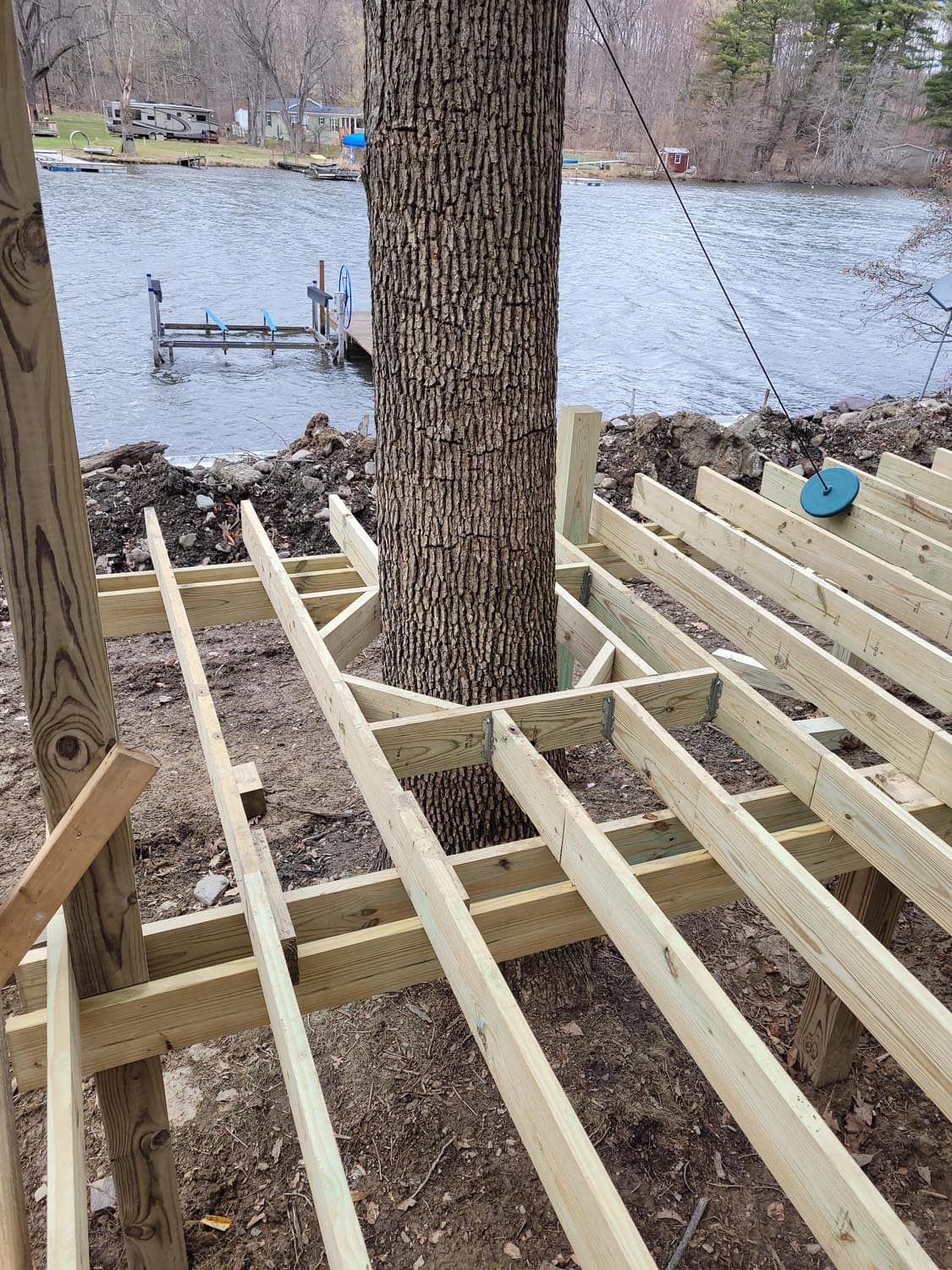 Wooden deck frame construction built around large tree trunk near lake