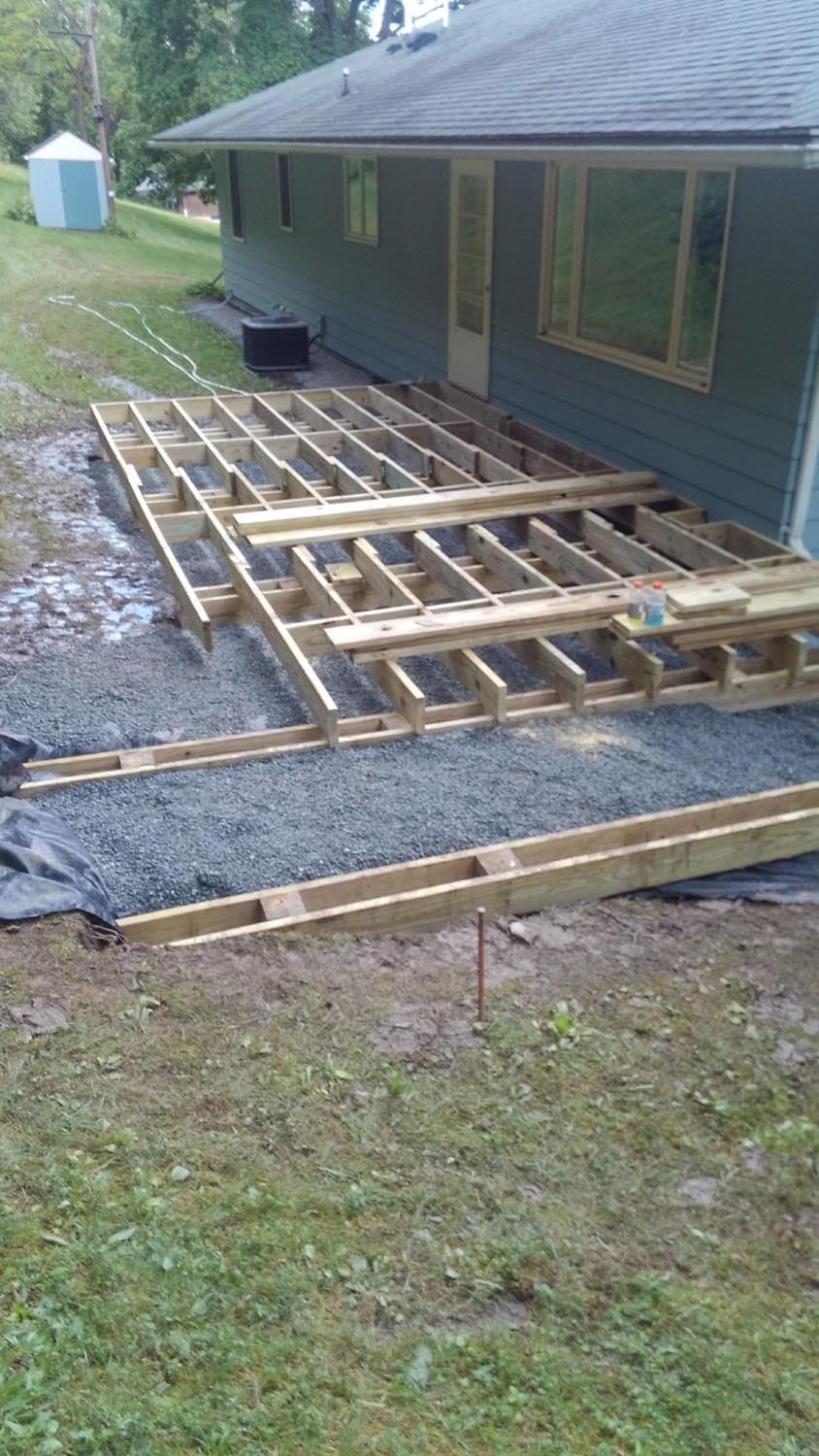 Wooden deck frame under construction on gravel base next to house