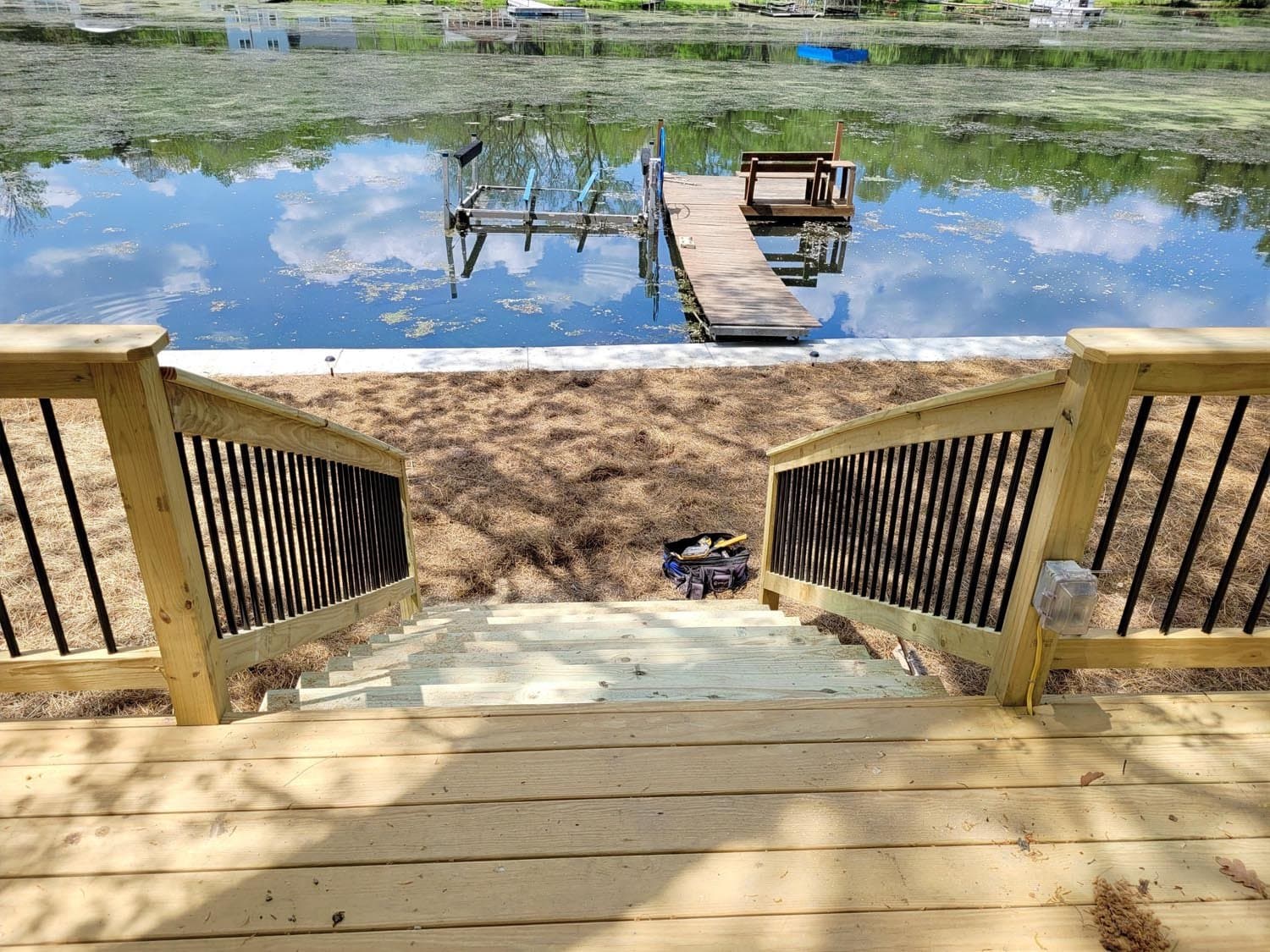 Wooden deck stairs leading to sandy shore with dock extending into lake