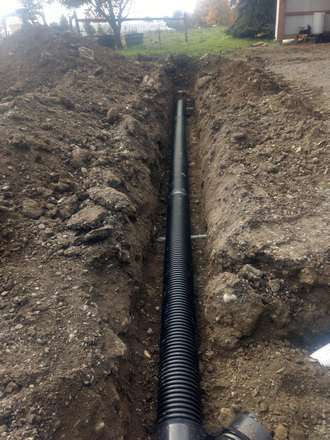 Black corrugated drainage pipe installed in excavated trench