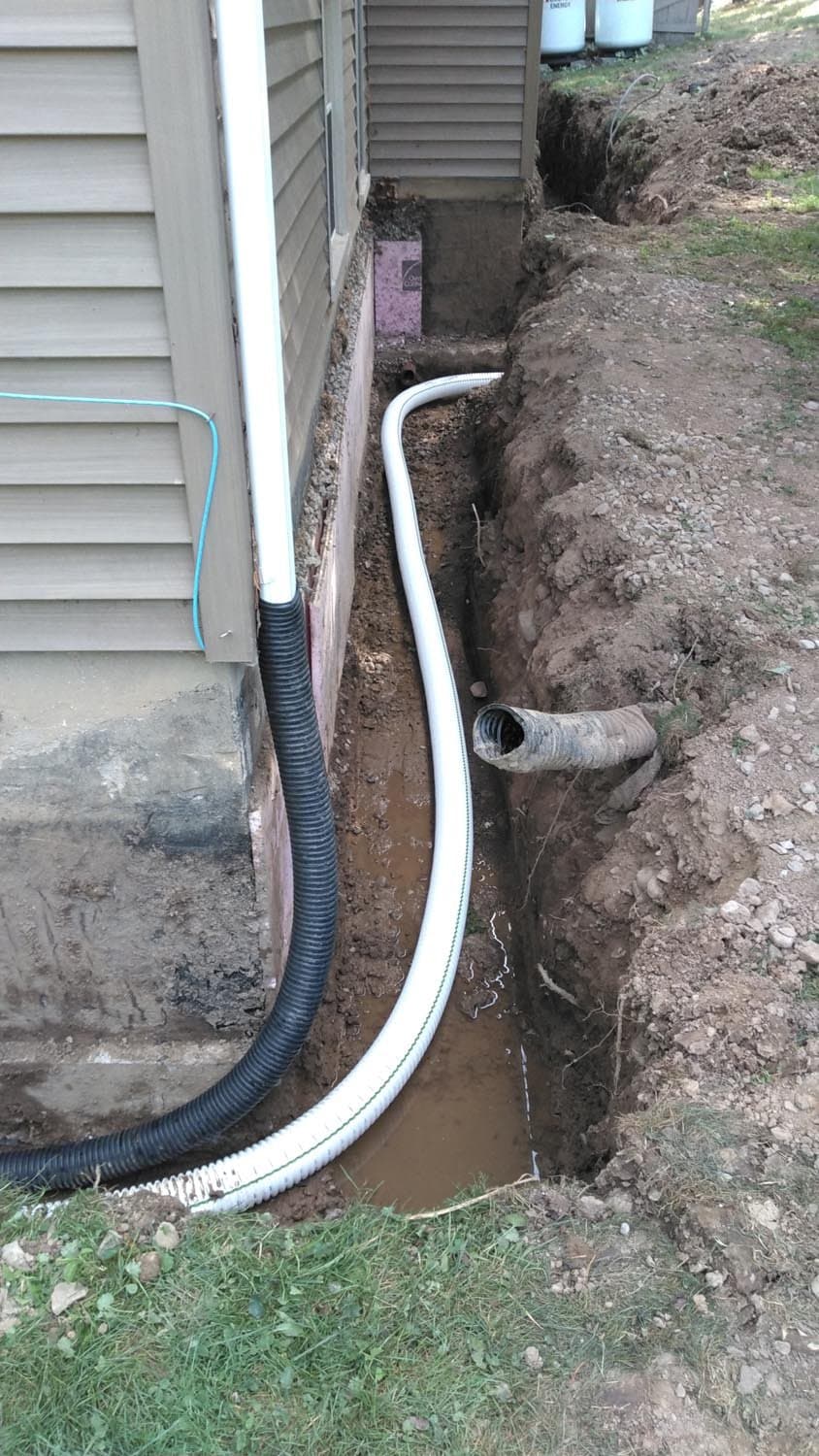 White drainage pipes installed in trench along house foundation