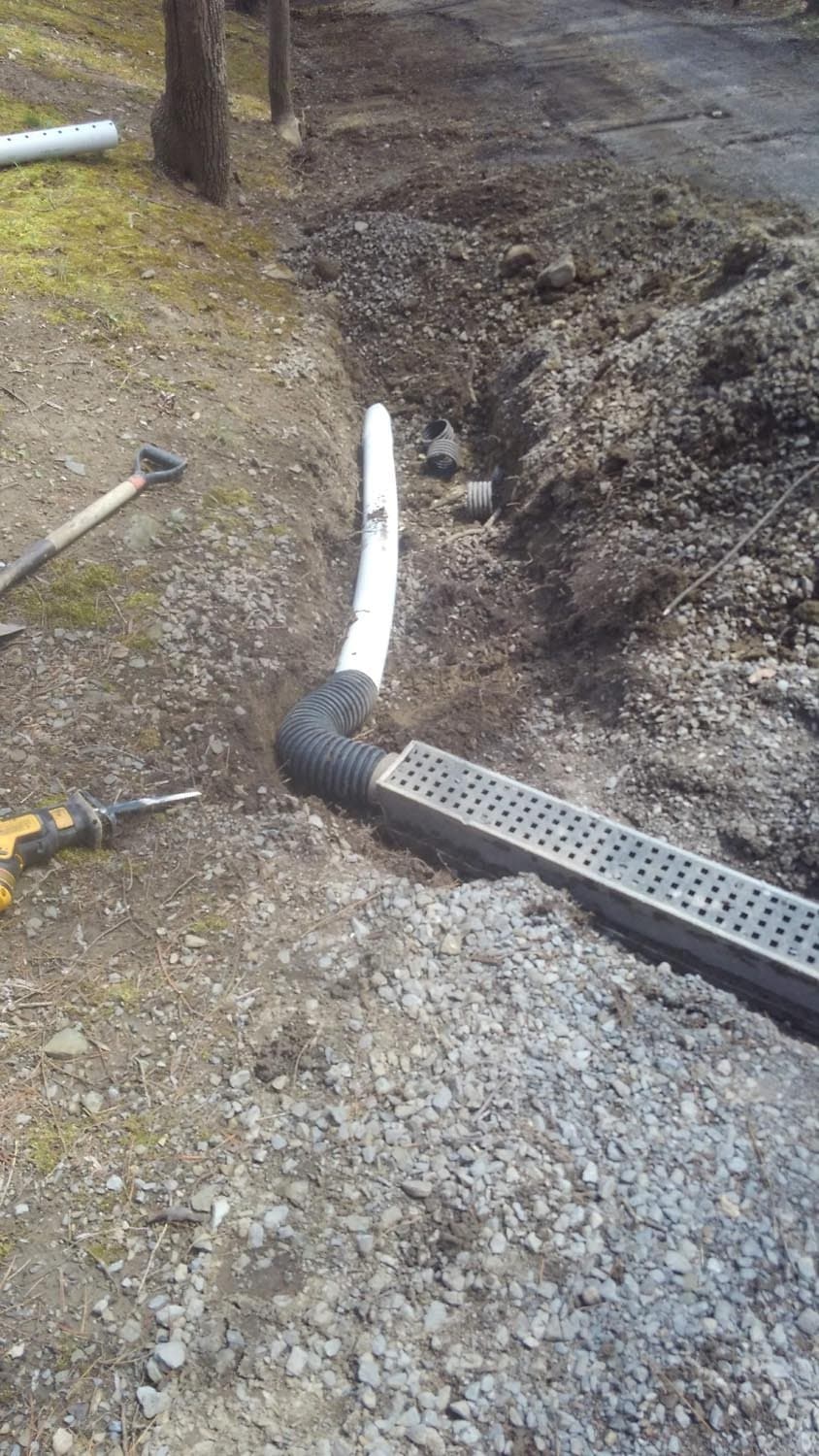 White drainage pipe and channel drain installed in gravel trench alongside driveway