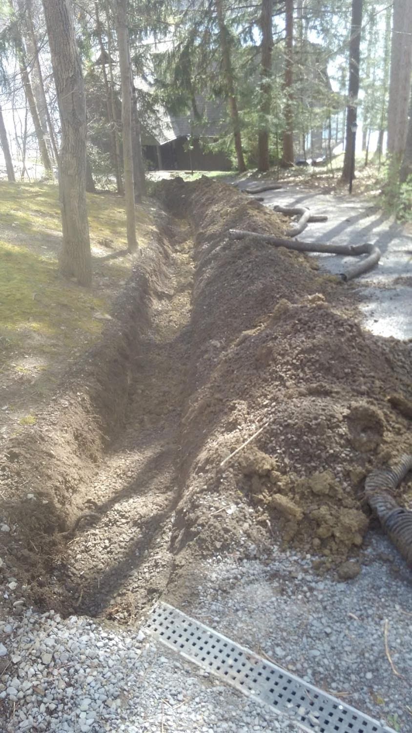 Excavated drainage trench with corrugated pipes and gravel bed in wooded area