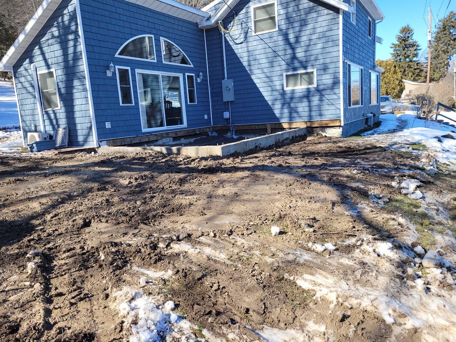 Blue house on concrete foundation with excavated muddy ground in front