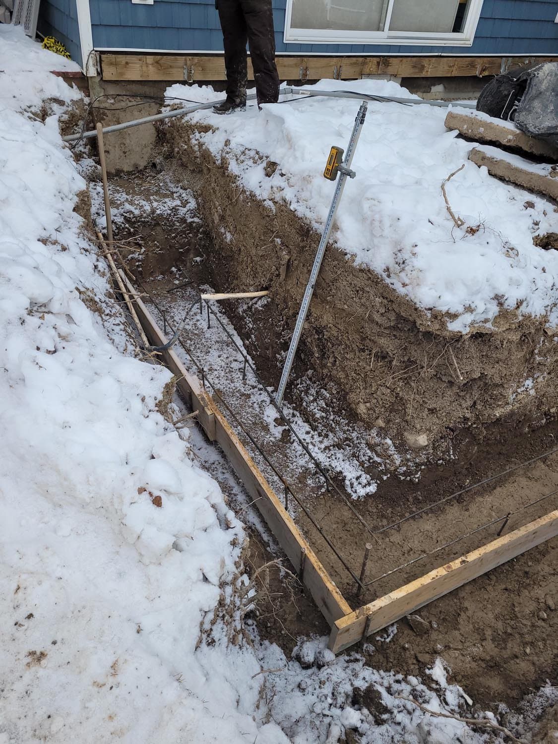 Wooden foundation forms with rebar set in excavated area with snow