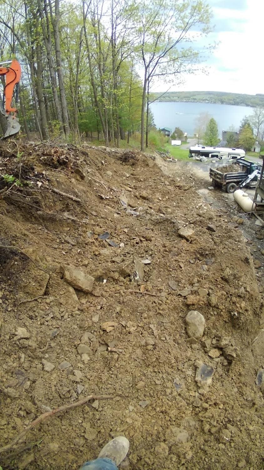 Excavated foundation site overlooking Finger Lakes with equipment and trees