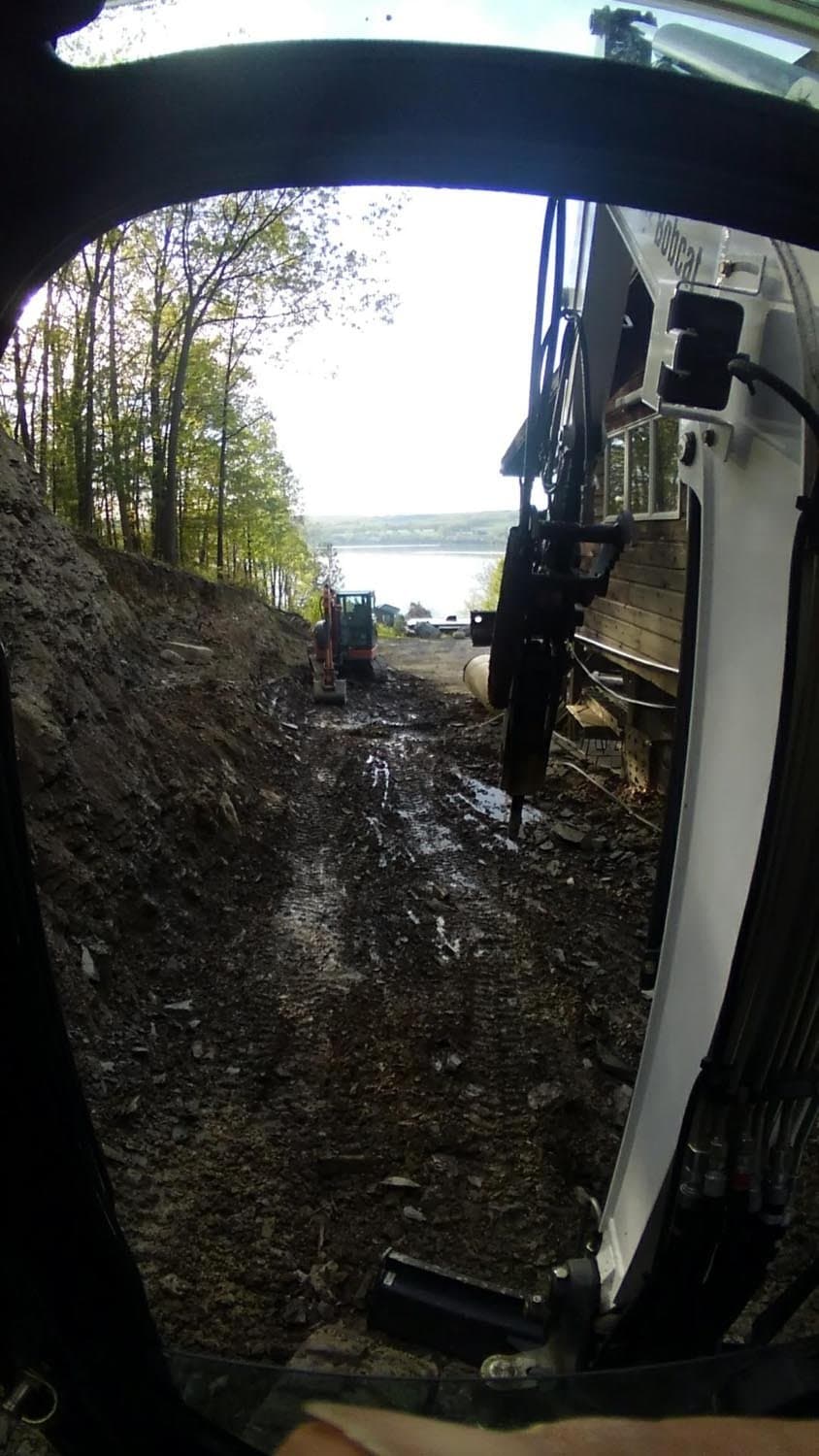 View from excavator cabin working on foundation site near lake with trees