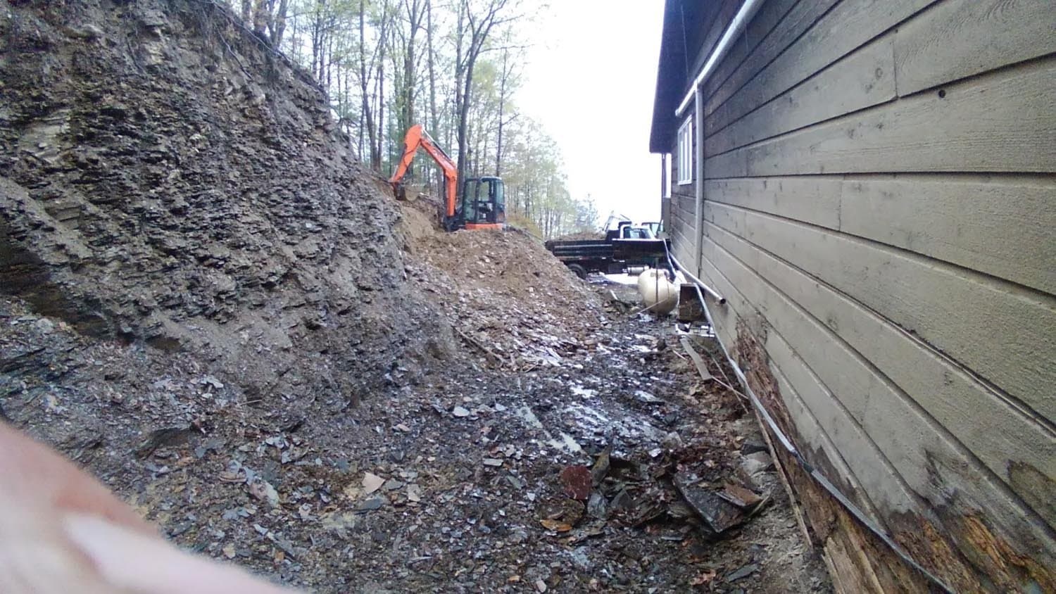 Orange excavator working on hillside foundation excavation next to building