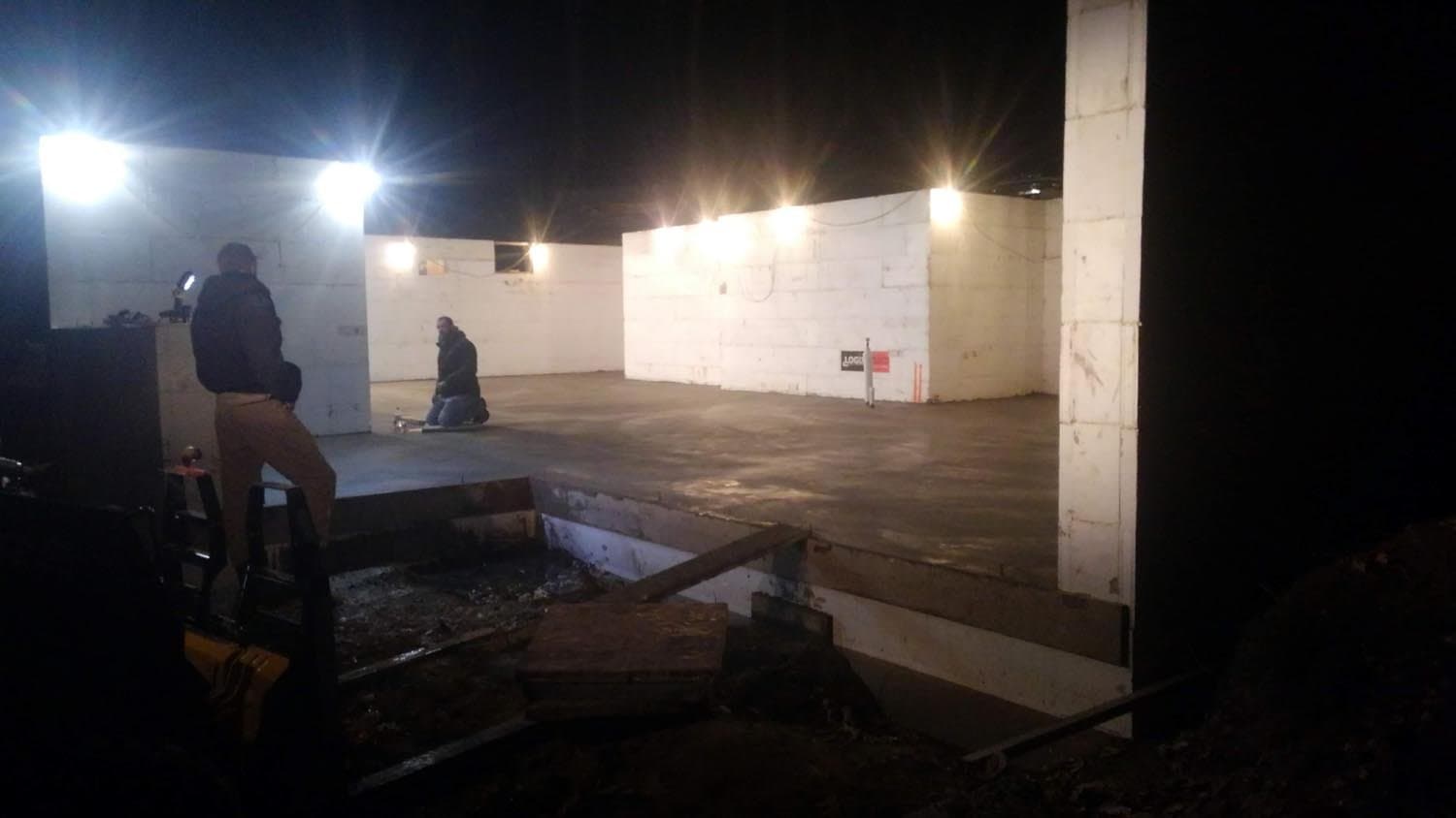 Workers inspecting concrete foundation under construction lighting at night