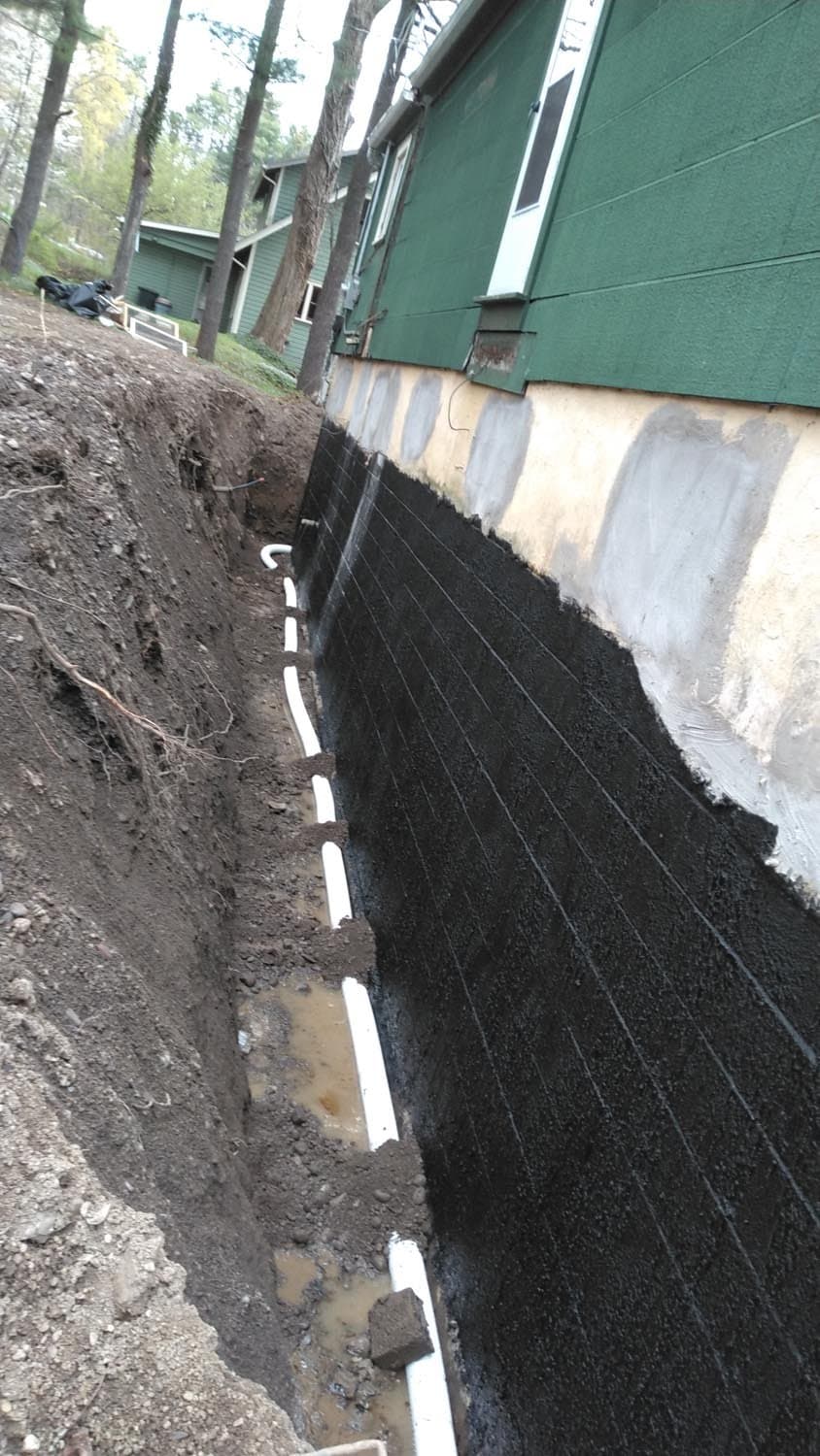 Black waterproofing membrane applied to concrete foundation wall with white drainage board