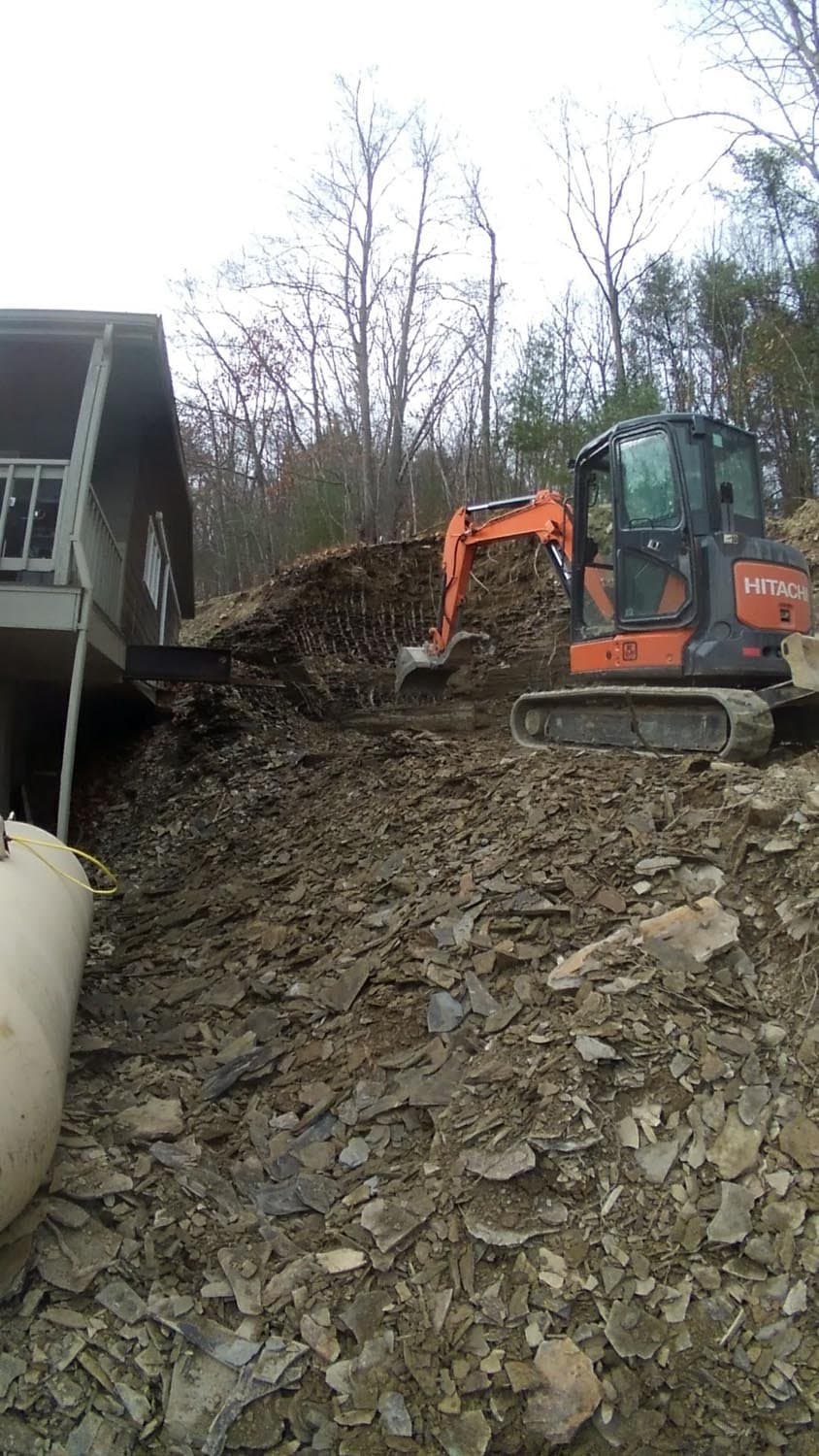 Orange Hitachi excavator digging foundation next to residential building