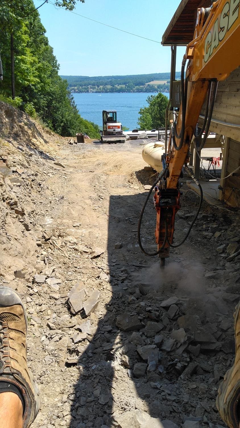 Excavator digging foundation site on hillside with lake view