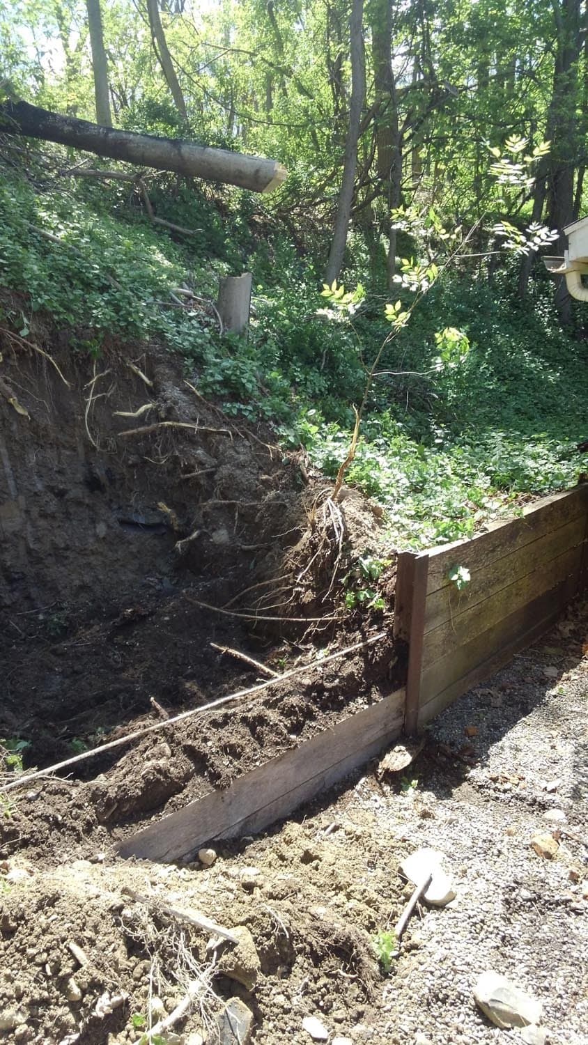 Wooden retaining wall being installed along excavated hillside with exposed roots and soil