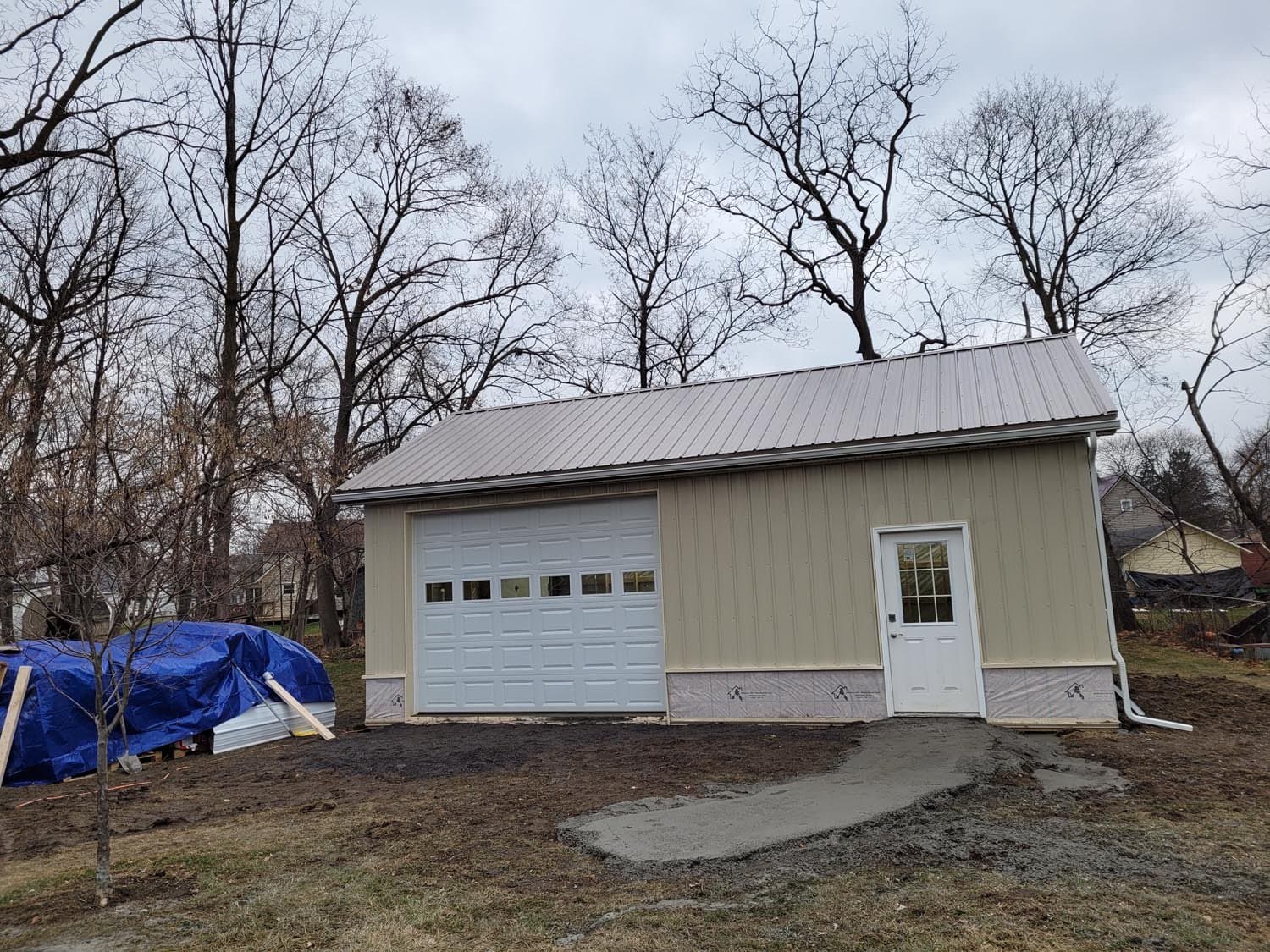 Beige pole barn with metal roof, white garage door, and side entry door