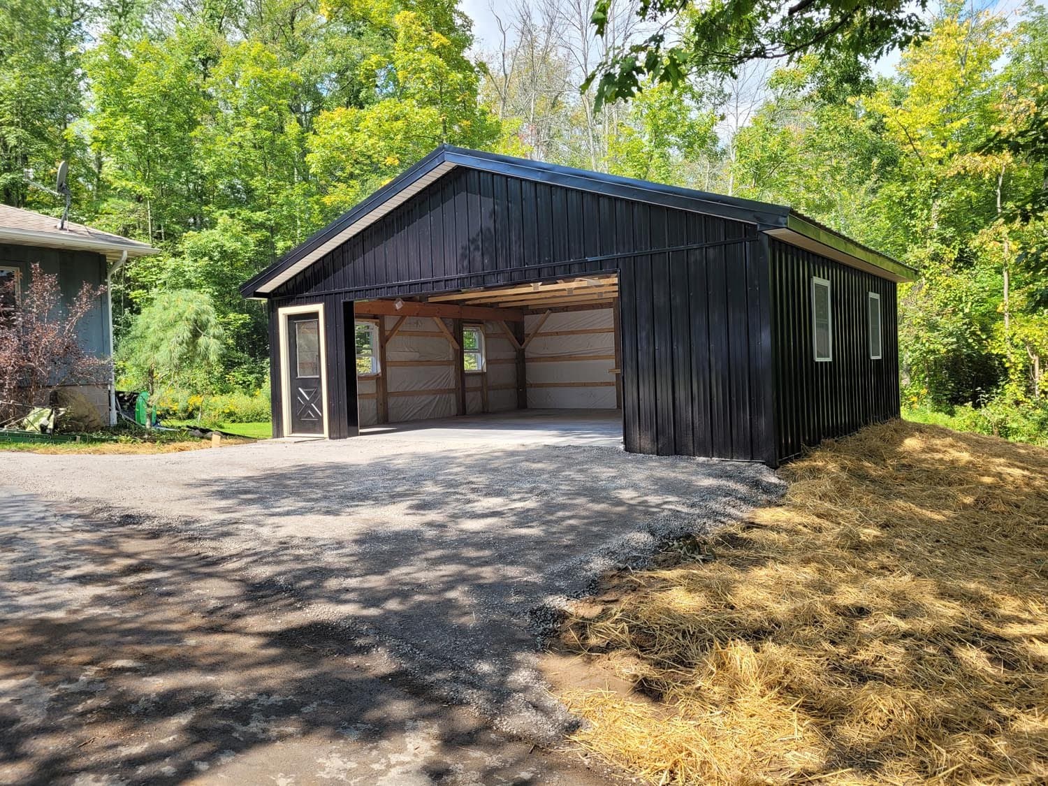 Black vertical siding pole barn with open garage door showing timber frame structure