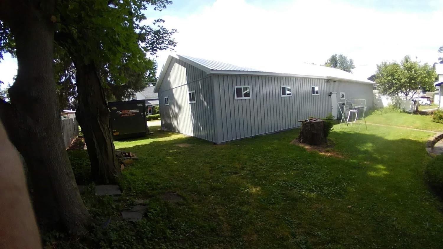White metal pole barn with multiple windows on residential property