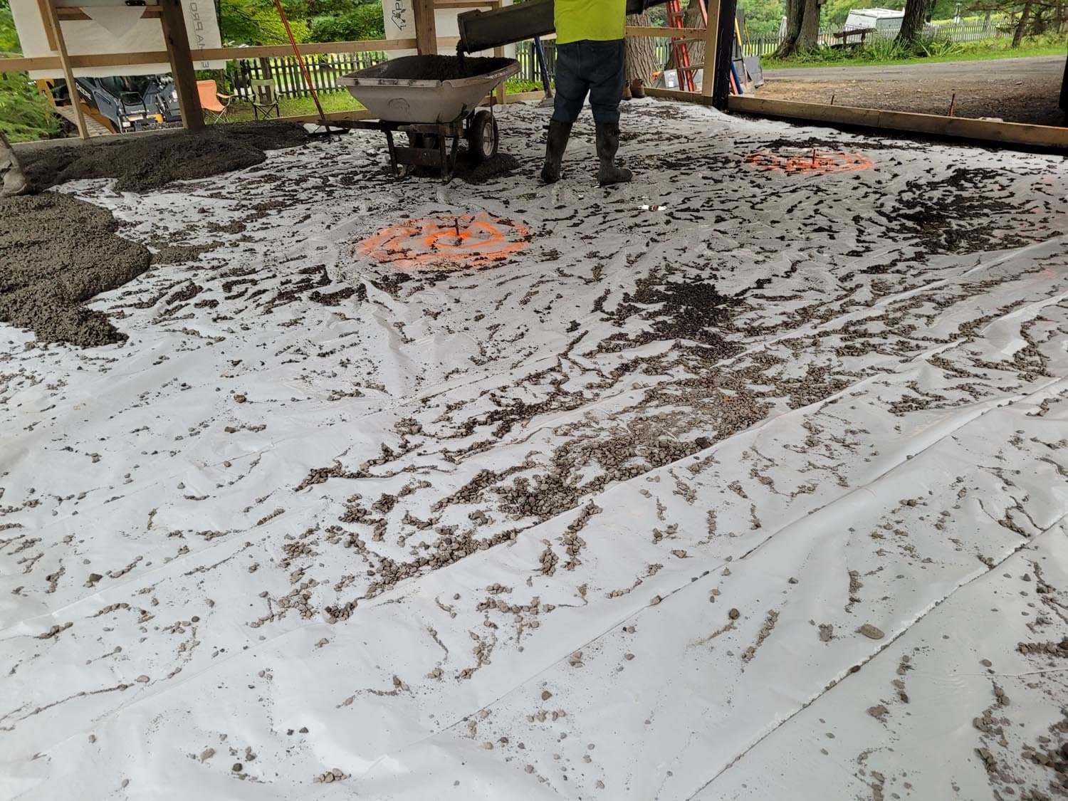 Fresh concrete slab with orange spray paint markings and wheelbarrow during pole barn construction