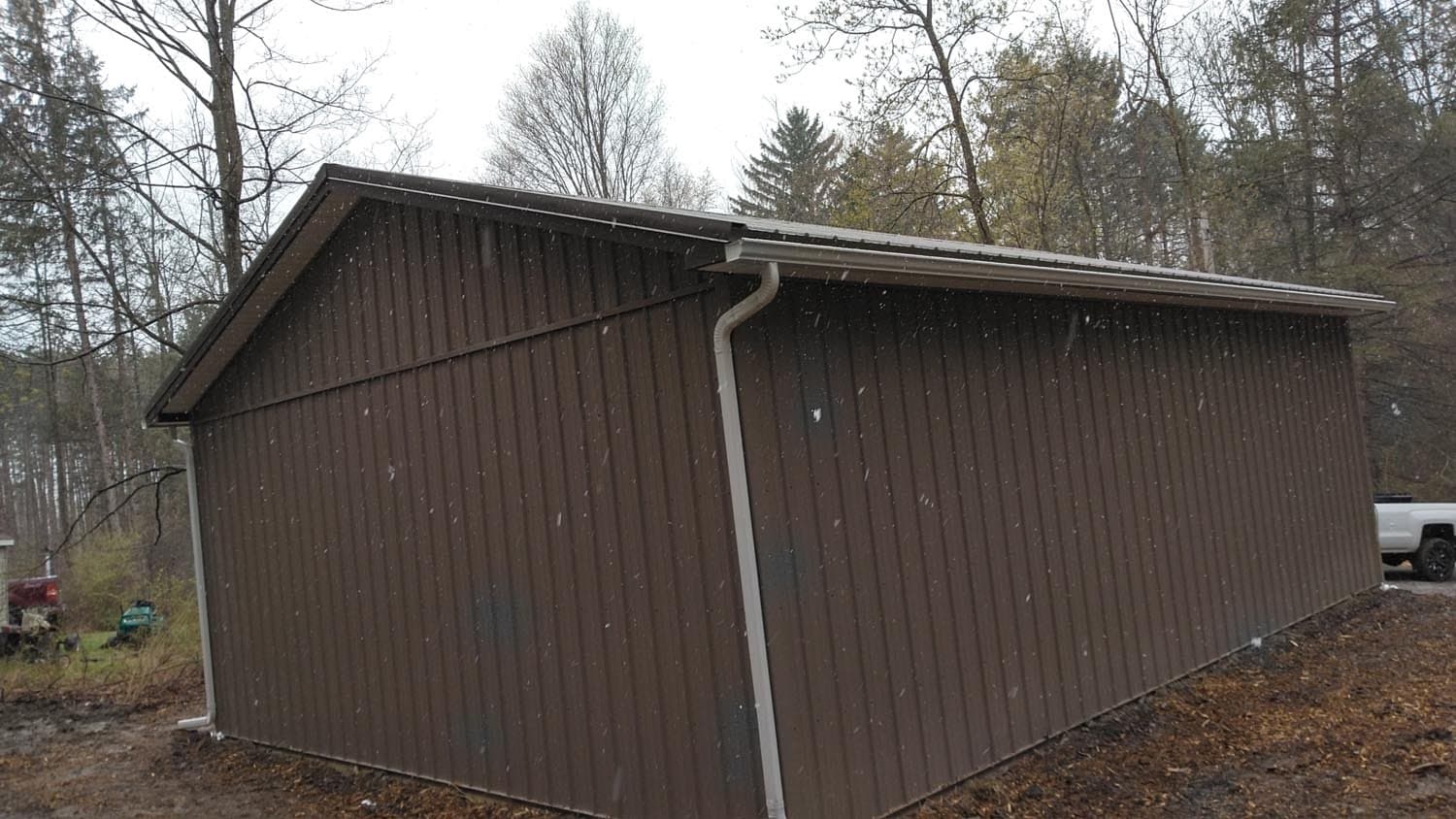 Dark brown vertical wood siding pole barn with white downspout and trim
