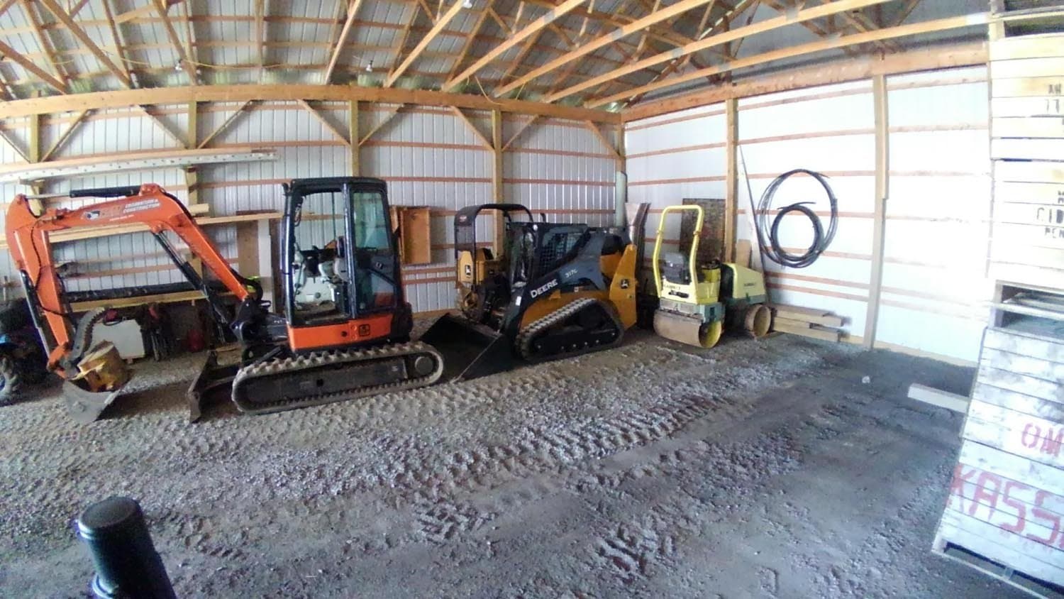 Construction equipment including excavators and skid steer stored inside pole barn