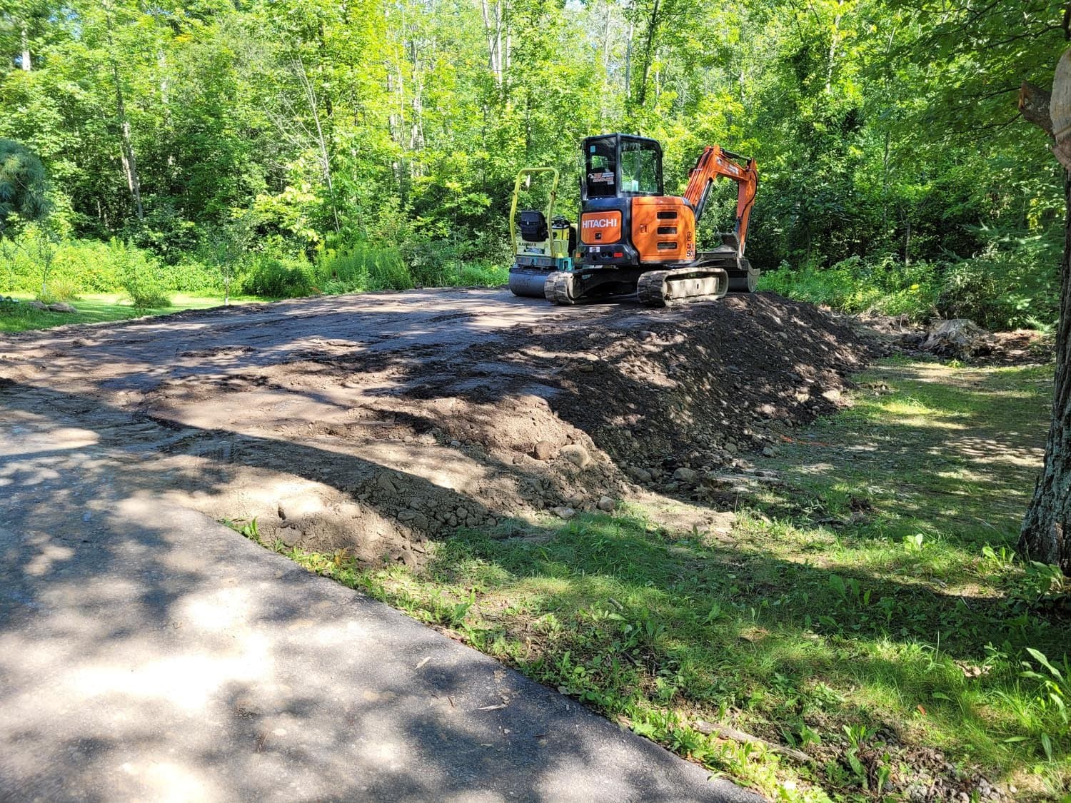 Orange excavator and blue compactor preparing ground for pole barn construction