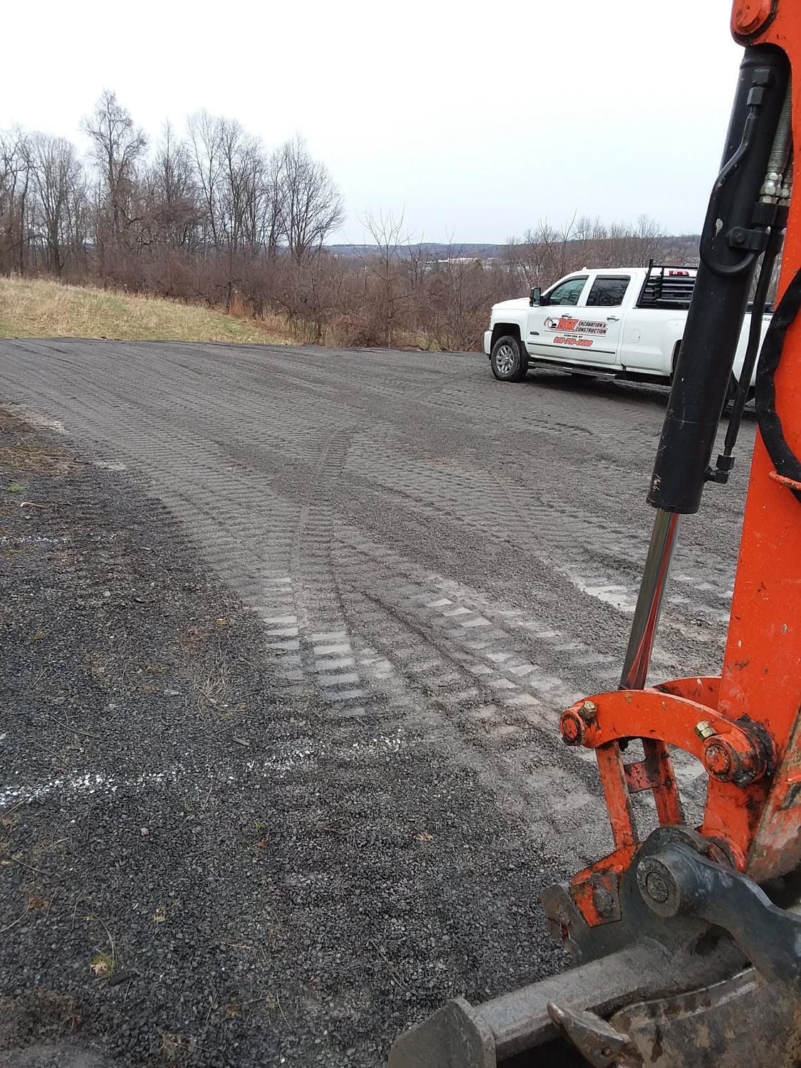 Excavator bucket and white pickup truck on gravel site prepared for pole barn construction