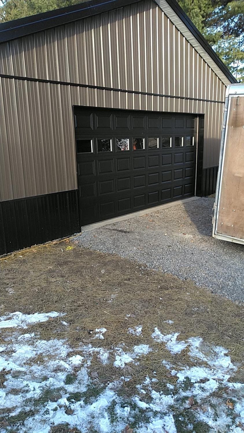 Completed pole barn with tan metal siding and black garage door with windows