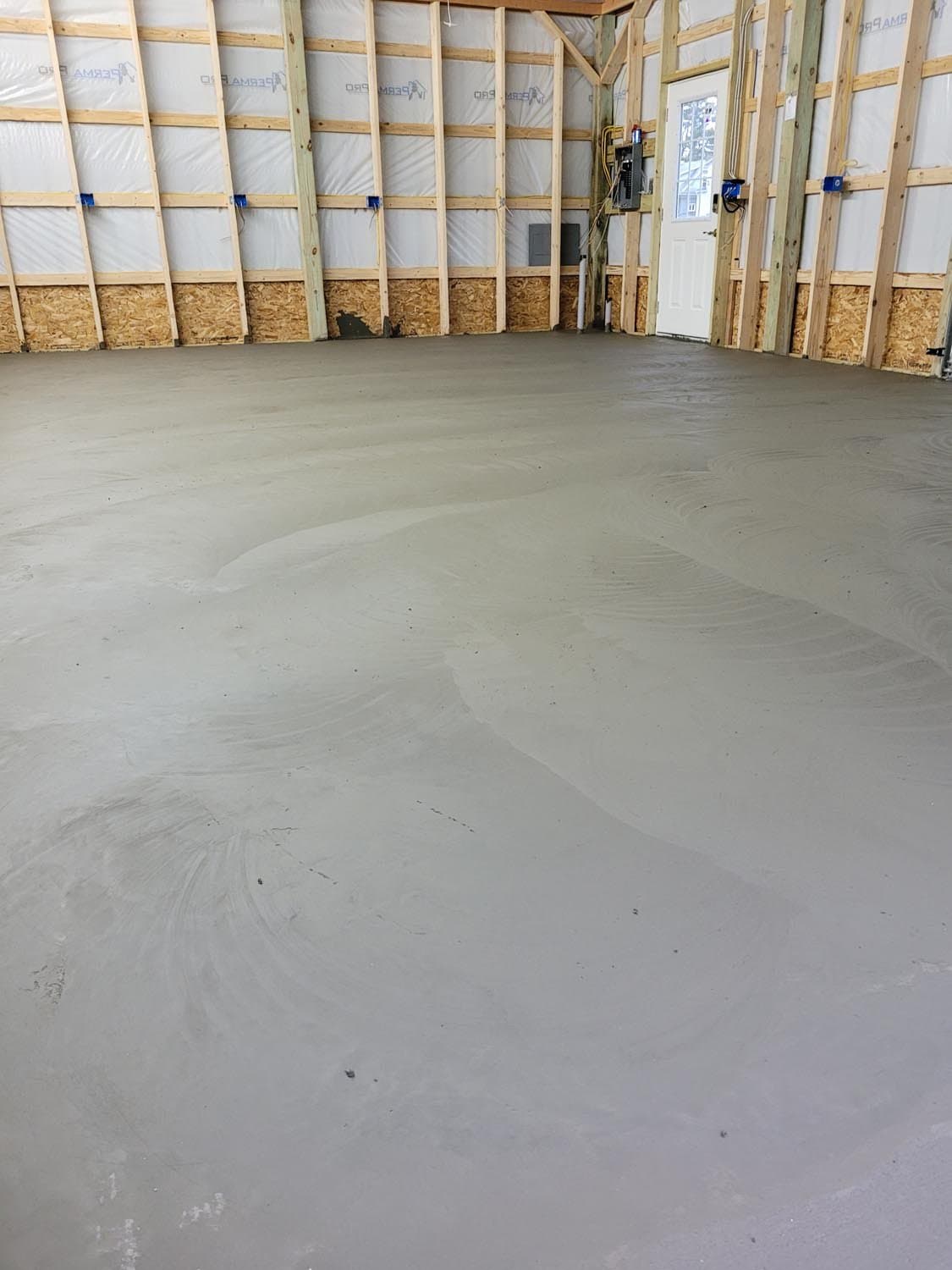 Freshly poured concrete floor in pole barn under construction with exposed wood framing