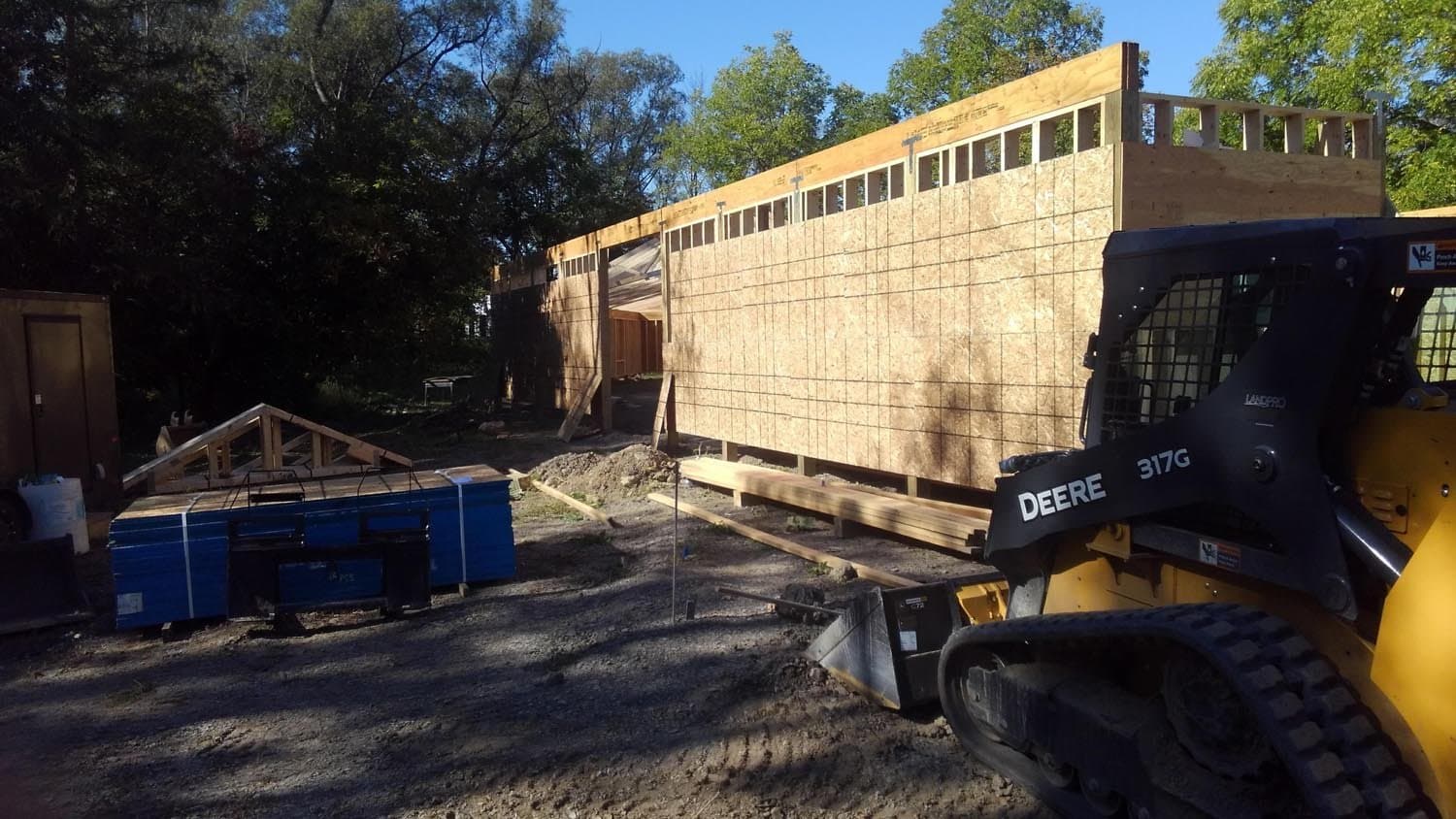 Pole barn under construction with plywood sheathing and exposed framing, Deere skid steer on site