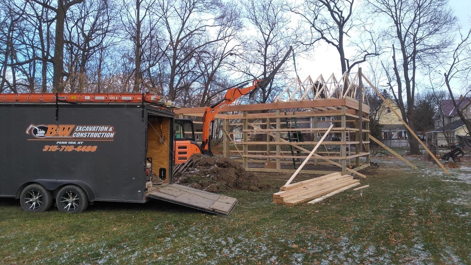 Wooden pole barn frame under construction with excavator and BW Excavation trailer
