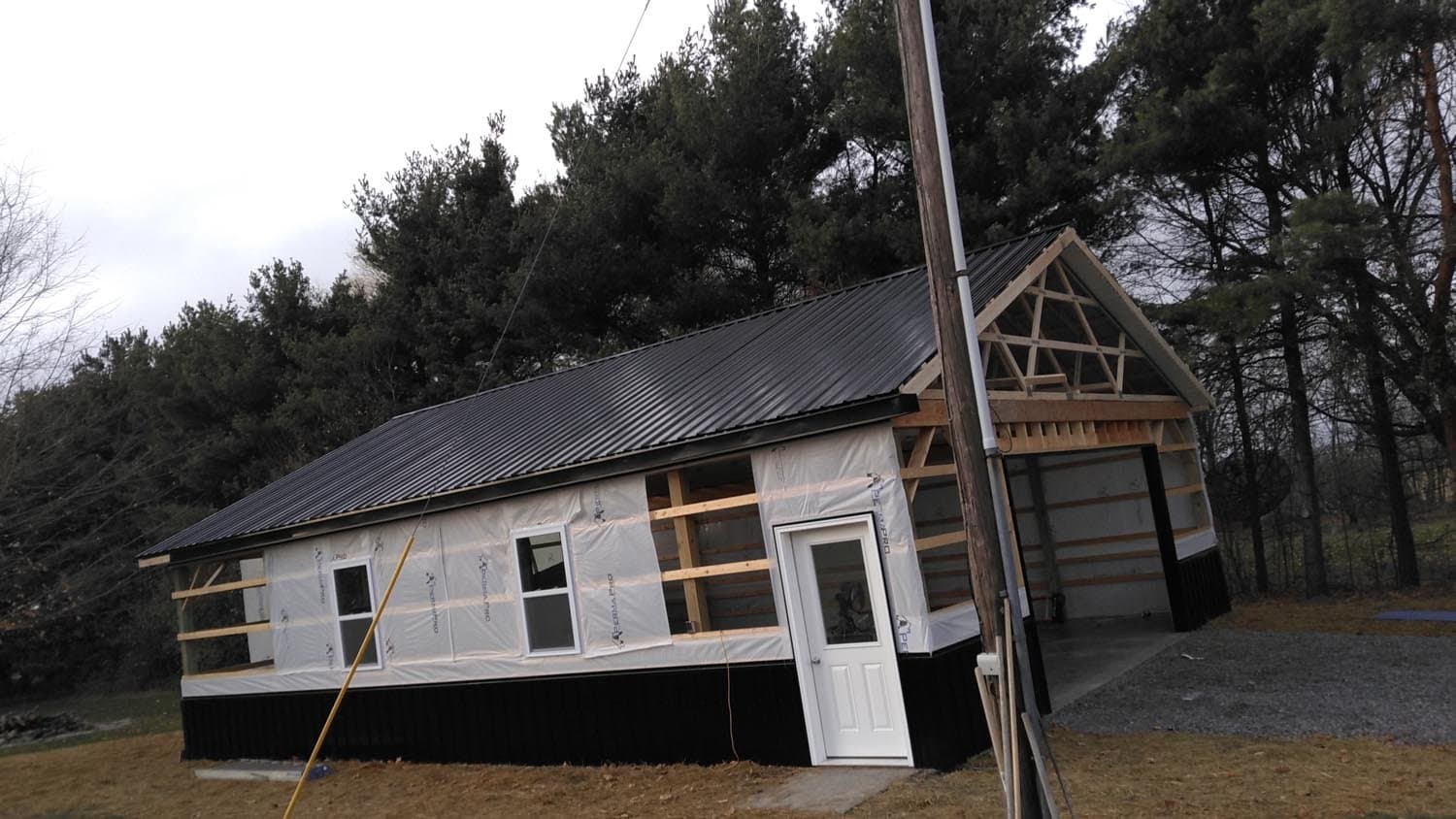 Pole barn under construction with metal roofing and house wrap siding