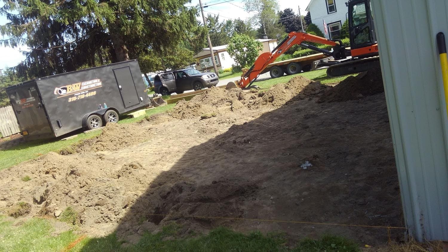 Orange excavator digging foundation for pole barn construction in residential yard