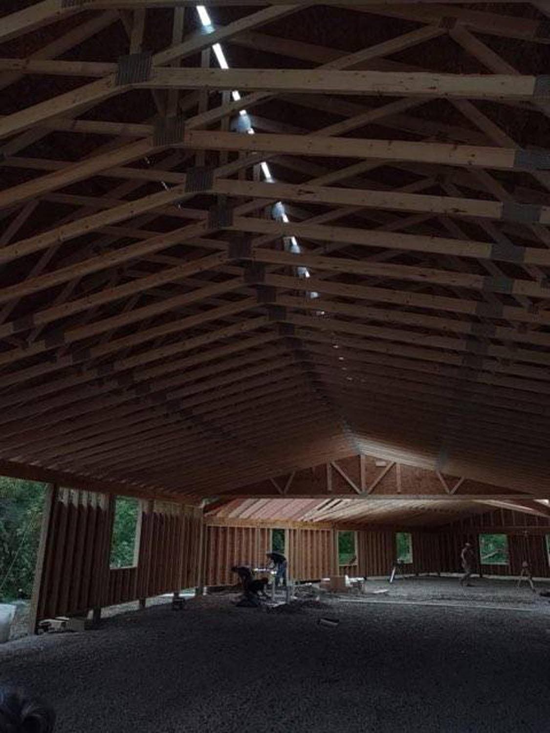 Interior of pole barn under construction showing exposed wooden truss roof system