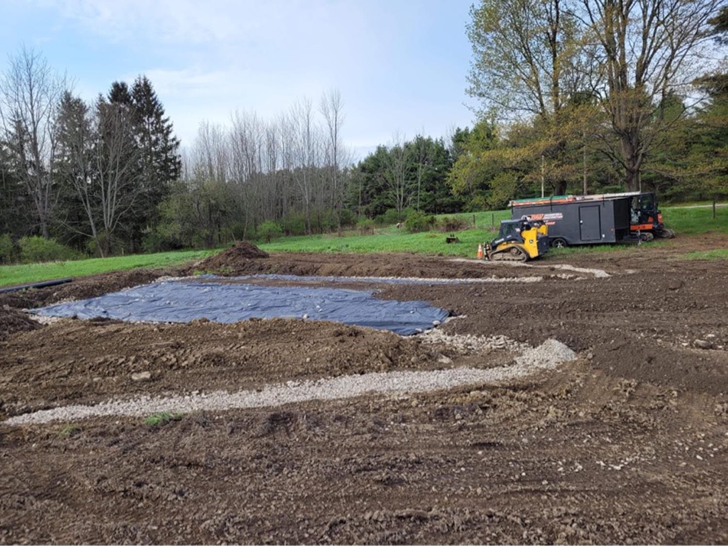 Skid steer grading foundation site with blue liner and gravel base for pole barn construction