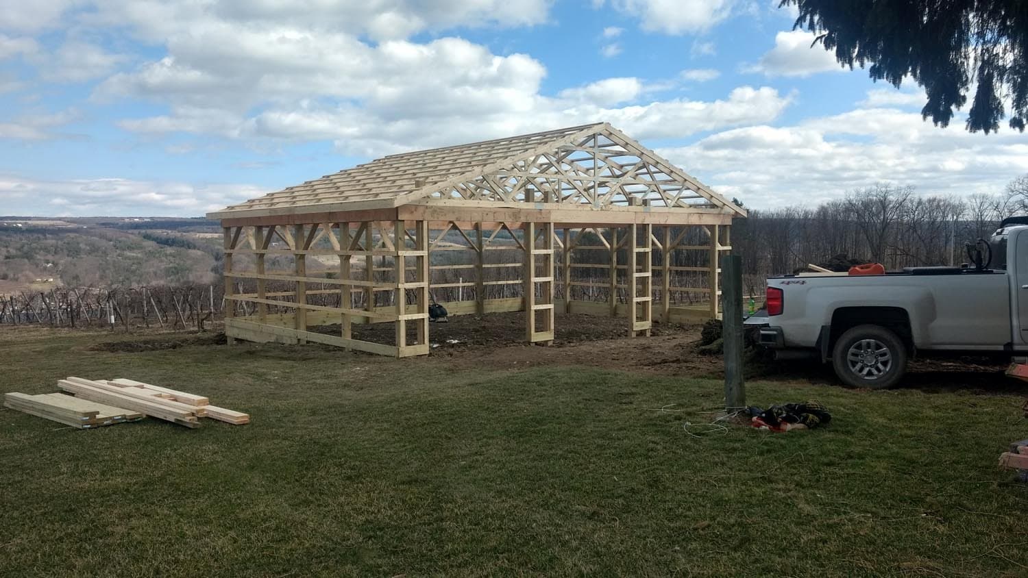 Wooden pole barn frame under construction with exposed roof trusses on rural property