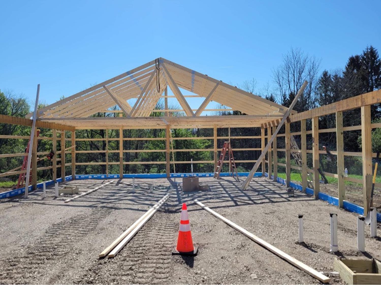 Wooden pole barn frame under construction with exposed roof trusses and foundation