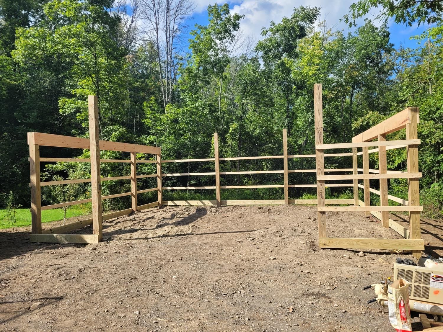 Wooden pole barn frame under construction with dirt foundation and forest backdrop
