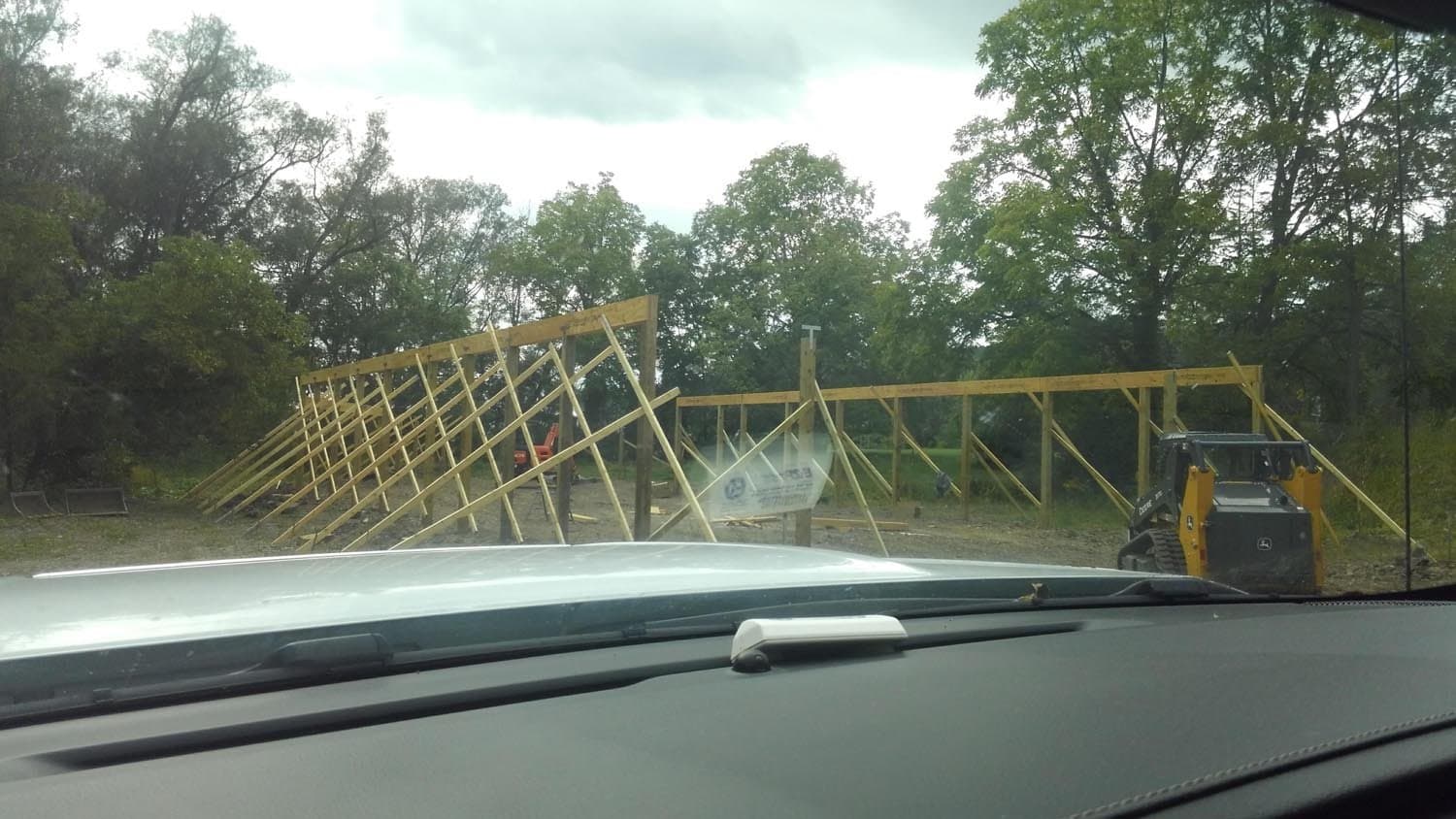 Wooden pole barn frame under construction with yellow skid steer loader on site