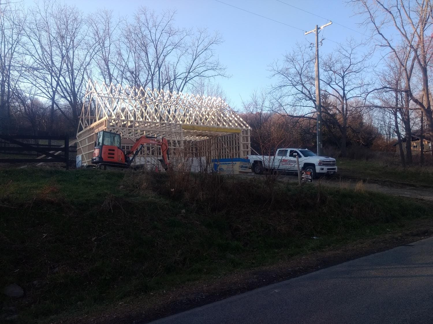 Wooden frame of pole barn under construction with excavator and trucks on site