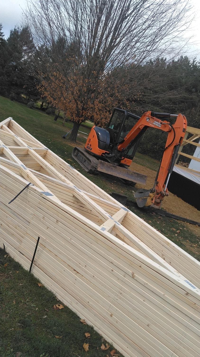 Pole barn roof trusses under construction with orange excavator in background