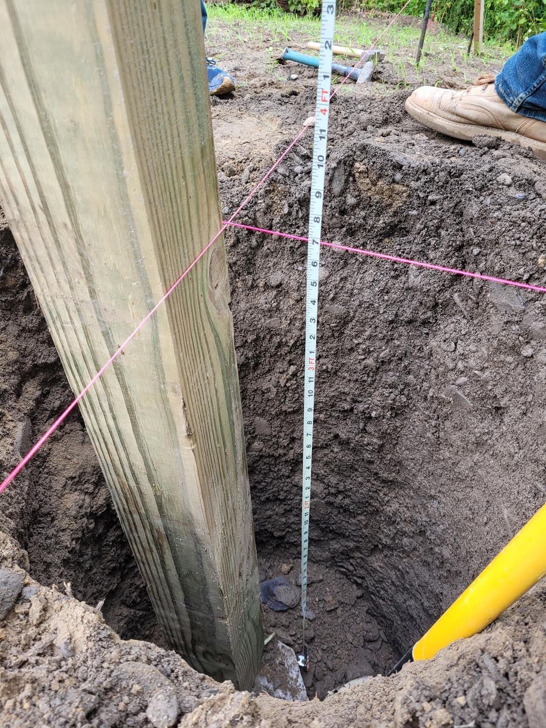 Measuring tape showing depth of wooden post hole for pole barn foundation