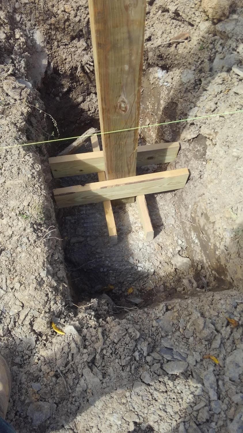 Vertical wooden post with cross bracing in excavated foundation hole