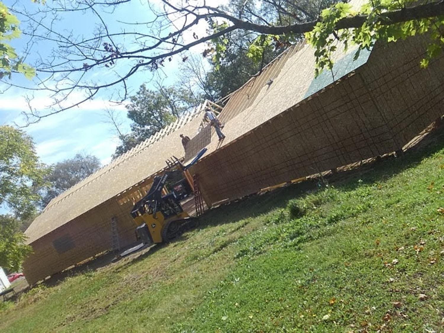Workers installing roofing on a pole barn under construction on a hillside