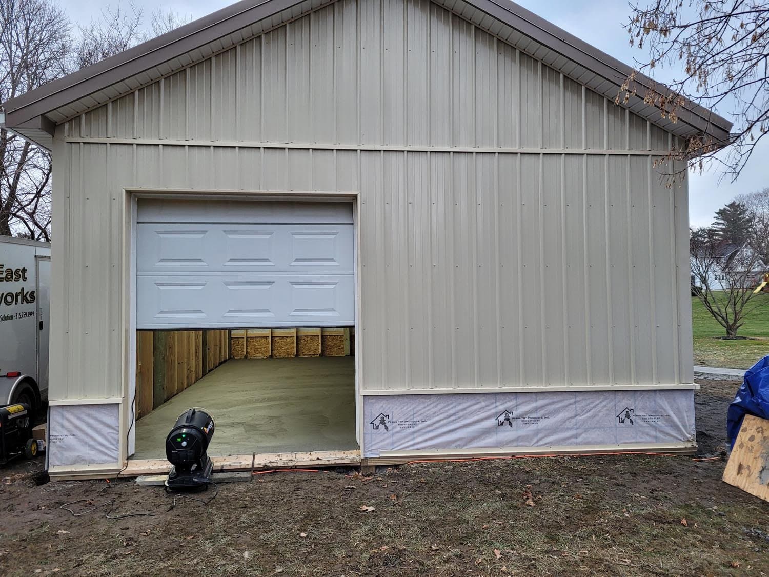 Pole barn with white garage door partially open showing interior construction