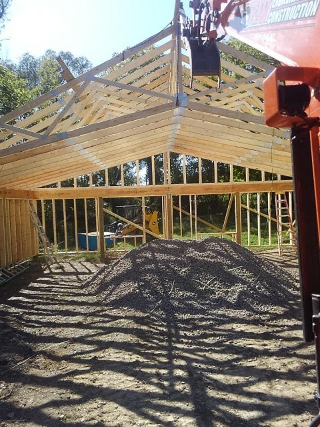 Wooden pole barn frame under construction with exposed roof trusses and gravel floor