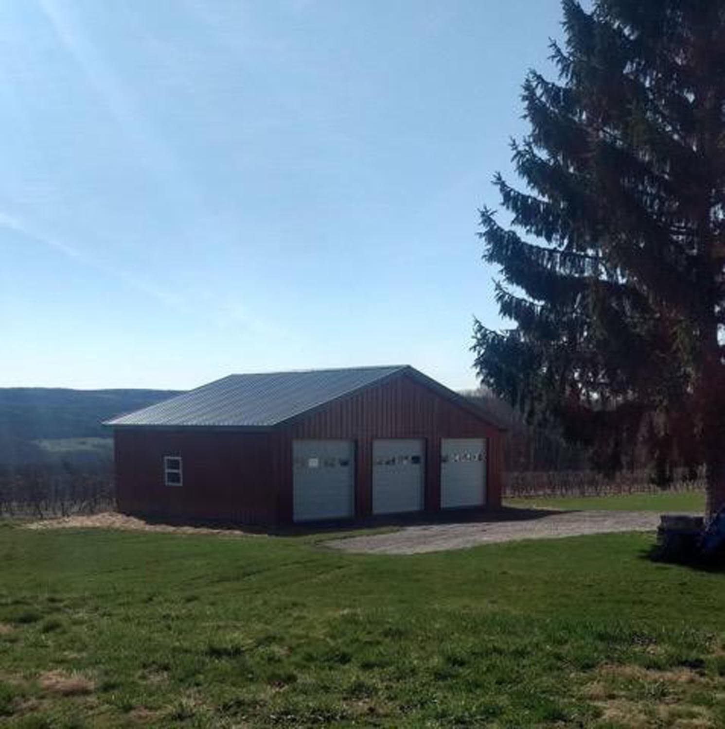 Red pole barn with three white garage doors and metal roof in rural setting